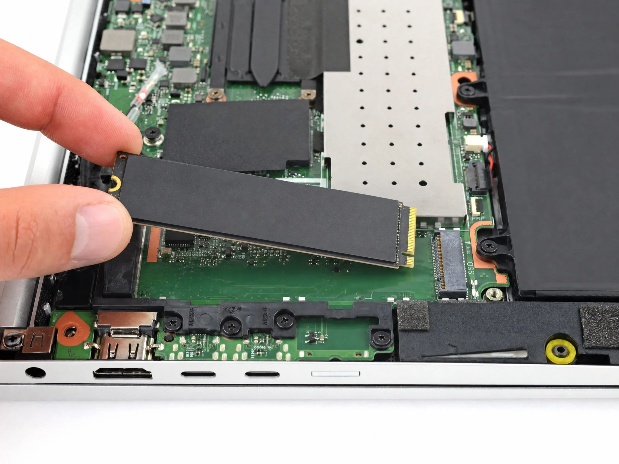 Hand removing an M.2 SSD from the motherboard of an opened HP EliteBook laptop during a repair